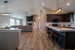 Kitchen with a center island, a fireplace, light wood-type flooring, ceiling fan with notable chandelier, and black range oven