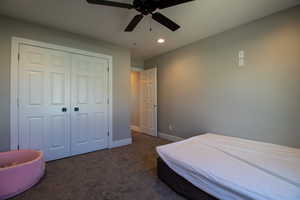 Bedroom with dark carpet, ceiling fan, and a closet