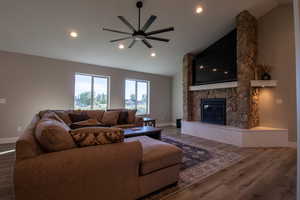 Living room with lofted ceiling, wood-type flooring, ceiling fan, and a stone fireplace