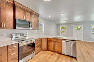 Kitchen featuring appliances with stainless steel finishes, kitchen peninsula, sink, and light hardwood / wood-style floors