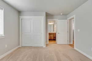 Unfurnished bedroom featuring ensuite bathroom, light colored carpet, and a closet