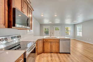 Kitchen with light hardwood / wood-style flooring, kitchen peninsula, stainless steel appliances, and sink