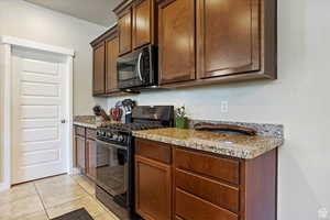 Kitchen with black gas range, light tile patterned floors, and light stone countertops