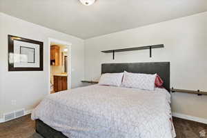 Bedroom with connected bathroom and dark colored carpet