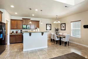 Kitchen featuring hanging light fixtures, light stone countertops, a notable chandelier, black refrigerator, and a kitchen breakfast bar