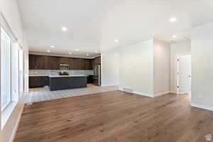 Kitchen with light wood-type flooring, appliances with stainless steel finishes, a kitchen island, and dark brown cabinets