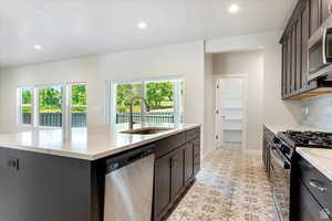 Kitchen with light tile patterned floors, stainless steel appliances, sink, decorative backsplash, and a kitchen island with sink