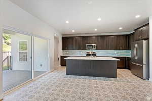 Kitchen with stainless steel appliances, sink, a kitchen island with sink, dark brown cabinets, and tasteful backsplash