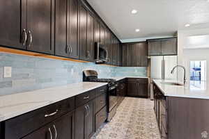 Kitchen with appliances with stainless steel finishes, light stone countertops, sink, decorative backsplash, and dark brown cabinetry