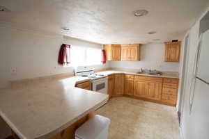 Kitchen featuring a textured ceiling, kitchen peninsula, sink, and white appliances