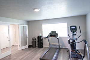 Workout room with light hardwood / wood-style floors, a textured ceiling, and french doors