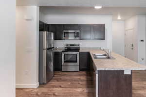 Kitchen with dark hardwood / wood-style floors, appliances with stainless steel finishes, kitchen peninsula, sink, and dark brown cabinetry