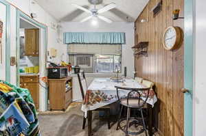 Carpeted dining space with a textured ceiling, ceiling fan, wood walls, and vaulted ceiling