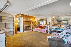 Bedroom featuring a textured ceiling, carpet flooring, ceiling fan, and wood walls