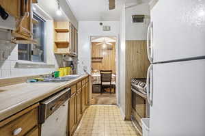 Kitchen with dishwasher, wooden walls, white fridge, electric stove, and decorative backsplash