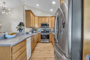 Kitchen with vaulted ceiling, decorative light fixtures, stainless steel appliances, light hardwood / wood-style floors, and a chandelier