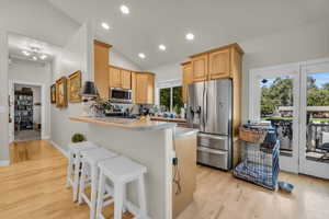 Kitchen featuring a kitchen bar, stainless steel appliances, kitchen peninsula, vaulted ceiling, and light hardwood / wood-style floors