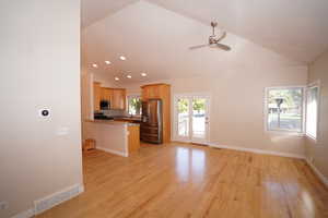 Kitchen featuring light wood-type flooring, lofted ceiling, kitchen peninsula, appliances with stainless steel finishes, and ceiling fan