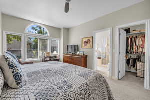 Bedroom with a spacious closet, a closet, ensuite bath, light colored carpet, and ceiling fan