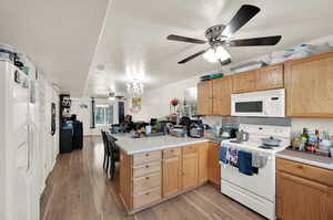 Kitchen featuring white appliances, light brown cabinetry, light hardwood / wood-style floors, kitchen peninsula, and ceiling fan