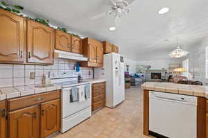 Kitchen featuring ceiling fan with notable chandelier, white appliances, tile countertops, and a textured ceiling