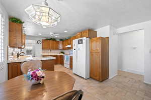 Kitchen featuring a textured ceiling, white appliances, tasteful backsplash, kitchen peninsula, and sink