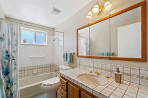 Full bathroom featuring backsplash, shower / bathtub combination with curtain, toilet, vanity, and a textured ceiling