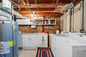 Washroom featuring gas water heater, sink, cabinets, and separate washer and dryer