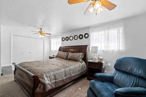 Carpeted bedroom with a textured ceiling, ceiling fan, and a closet