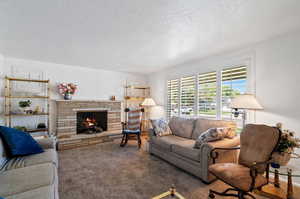 Living room featuring a textured ceiling, carpet, and a stone fireplace