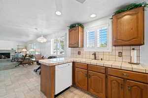 Kitchen featuring white dishwasher, kitchen peninsula, tile countertops, and decorative backsplash