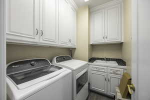 Laundry room with dark hardwood / wood-style flooring, cabinets, washing machine and dryer, and sink