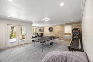 Rec room with ornamental molding, light carpet, a textured ceiling, and wooden walls