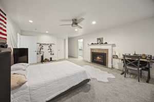 Bedroom with ceiling fan, light colored carpet, and a tile fireplace