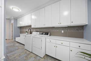 Laundry area featuring washer and clothes dryer, sink, cabinets, and ornamental molding