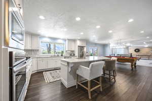 Kitchen featuring dark wood-type flooring, an island with sink, pool table, and a breakfast bar