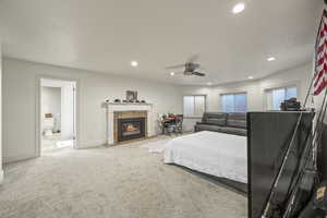 Bedroom with multiple windows, ceiling fan, a tile fireplace, and light carpet