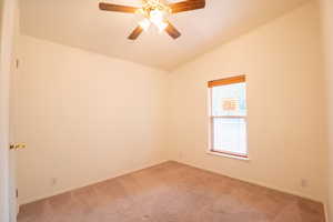 Empty room with ceiling fan, carpet floors, and vaulted ceiling