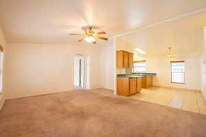 Unfurnished living room with ceiling fan with notable chandelier, light colored carpet, and vaulted ceiling