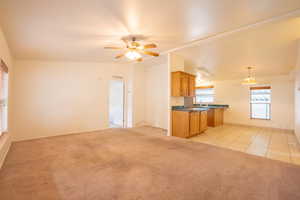 Kitchen featuring vaulted ceiling, ceiling fan with notable chandelier, light carpet, hanging light fixtures, and kitchen peninsula