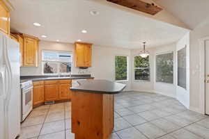 Kitchen featuring light tile patterned floors, white appliances, lofted ceiling, pendant lighting, and a kitchen island