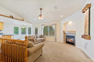 Carpeted living room with lofted ceiling, ceiling fan, and a tile fireplace