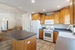 Kitchen with light tile patterned floors, a center island, white appliances, sink, and ceiling fan