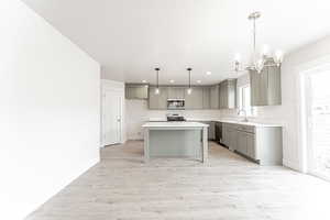 Kitchen with appliances with stainless steel finishes, gray cabinetry, light countertops, an inviting chandelier, and light wood finished floors