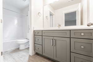 Bathroom with shower / tub combination, vanity, toilet, visible vents, and wood finished floors