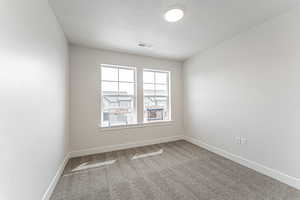 Carpeted empty room featuring a textured ceiling, visible vents, and baseboards