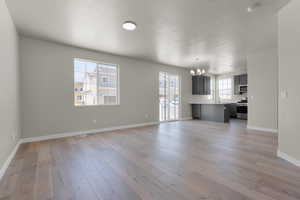 Unfurnished living room featuring a textured ceiling, light hardwood / wood-style flooring, and an inviting chandelier