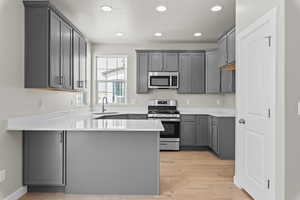 Kitchen with gray cabinets, stainless steel appliances, kitchen peninsula, and light wood-type flooring