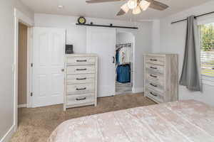 Carpeted bedroom with ceiling fan, a barn door, and a closet