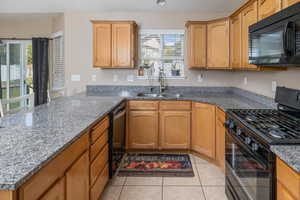 Kitchen with plenty of natural light, black appliances, sink, and stone countertops